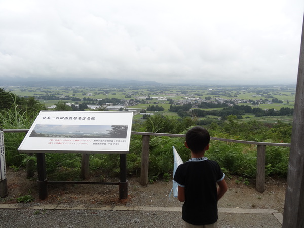 田園散居集落展望台から見渡す田んぼと山々の景色、案内板と子供の後ろ姿