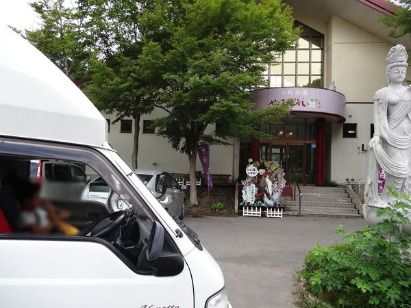 小町の湯やまぼうしの入口前に停めた軽キャンピングカーと観音像