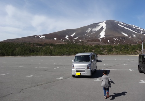 残雪が残る浅間山と軽キャンピングカー、その前を歩く子供